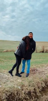 Couple smiling in a green field under cloudy skies.