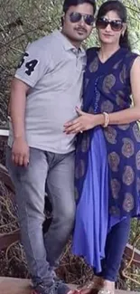 Couple posing on a deck in nature with green foliage.