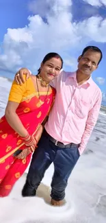 Couple standing on a scenic beach with waves and blue skies.