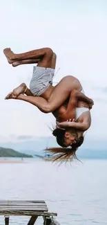 Couple performing an aerial flip over a tranquil body of water.