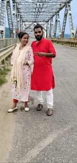 Couple stands on a scenic bridge in bright attire.