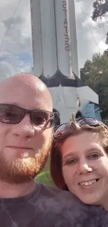 Couple taking a selfie with a large rocket in the background.