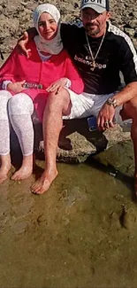 A couple sitting on rocks by the beach, enjoying the sun.