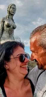 Couple smiling with a sculpture and blue sky.