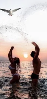 Couple enjoying sunset on the beach with water splashes and a flying bird overhead.