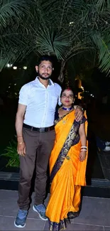 Couple standing under palm trees at night.