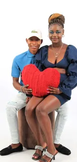 Couple holding a red heart pillow, dressed in blue.