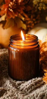 Glowing candle with autumn decor on cozy knit surface.