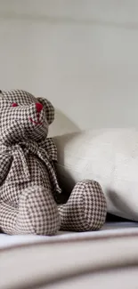 Teddy bear sitting on a neatly made bed with neutral tones.
