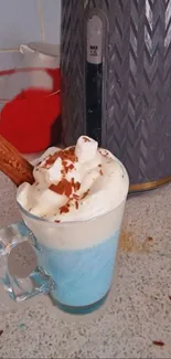 Blue hot chocolate with whipped cream and chocolate shavings in a glass mug.