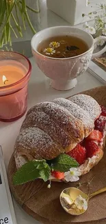 Cozy breakfast scene with croissant, strawberries, tea, and candle.