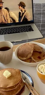 Cozy breakfast with pancakes and coffee in front of a laptop playing a movie.