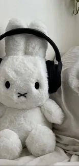 Cute plush bunny with headphones on a cozy bed.