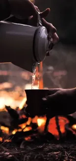 Hands pouring coffee by a campfire at dusk.