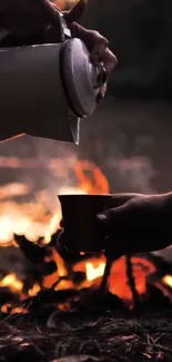 Hands pouring coffee by a campfire at dusk.