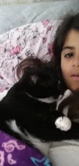 Child cuddling black and white cat in cozy floral-themed bedding.