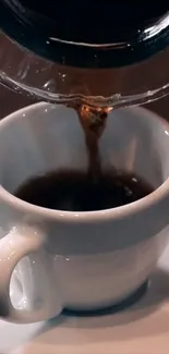 Coffee being poured into a white mug on a saucer.