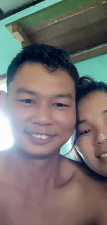 Smiling couple indoors with teal walls and wooden ceiling.