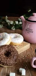 Cozy tea setting with donuts and pink teapot on a wooden table.