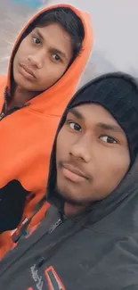 Two friends wearing hoodies taking a selfie outdoors.