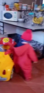 Child in red coat playing with yellow toy in kitchen.