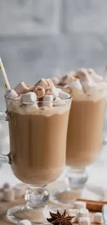 Two clear mugs of latte with marshmallows on top, set against a rustic backdrop.