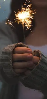 Hand holding sparkler with warm glow in a grey sweater.