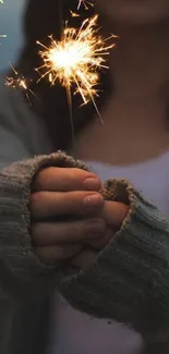 Cozy image of hands holding a sparkler with a dark, warm background.