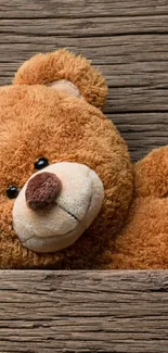 Cozy teddy bear resting on wooden planks wallpaper.