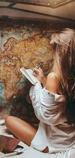 Woman writing in journal with world map in background.