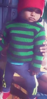 Child wearing a green striped sweater and red beanie.