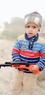 Adorable child in colorful winter clothes holding a toy gun outdoors.