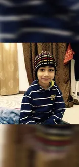 Smiling child in a cozy blue-striped sweater and colorful hat indoors.