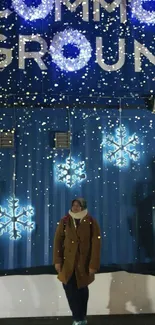 Person under glowing snowflake lights against a blue container wall at night.