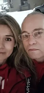 Selfie of two people in winter with snowy urban backdrop and red attire.