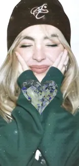 Smiling person in a beanie with a crystal heart on a green sweater.