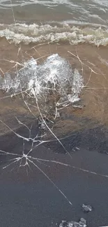 Cracked ice on sandy beach shore with ocean waves.