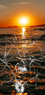 Cracked screen effect over sunset ocean view with orange glow.