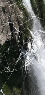 Cracked screen effect over a waterfall scene on phone wallpaper.