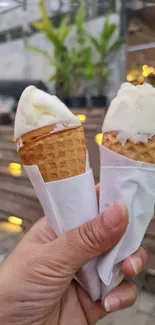 Hand holding two creamy ice cream cones outdoors.