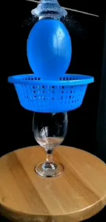 Blue water balloon setup with a colander and glass on a wooden table.