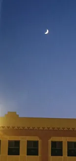 Crescent moon above a building at night, with a clear blue sky.