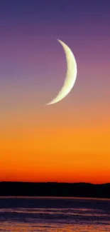 Crescent moon over ocean with colorful sunset sky.