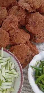 Crispy pakoras with green chillies and cucumber slices on a plate.