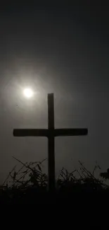 Silhouette of a cross against a dark sky with the setting sun.