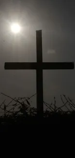 Silhouette of cross under bright sun on mobile wallpaper.