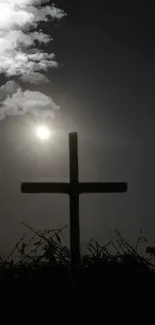 Silhouette of a cross against a sunset with clouds and a dark sky.