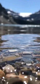 Serene mountain stream with clear water and pebbles under a bright blue sky.