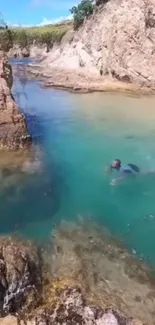 Swimmer in turquoise water by rugged cliffs.