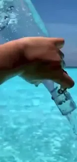 A hand pouring water into a vibrant turquoise ocean.